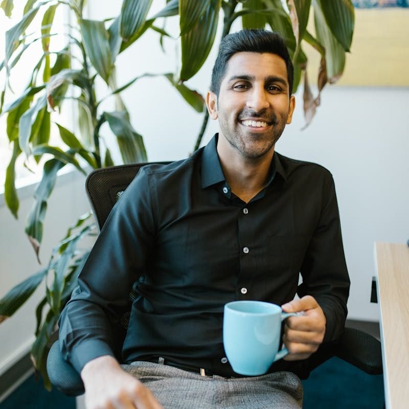 Cheerful man with coffee mug sitting in modern office with plant.